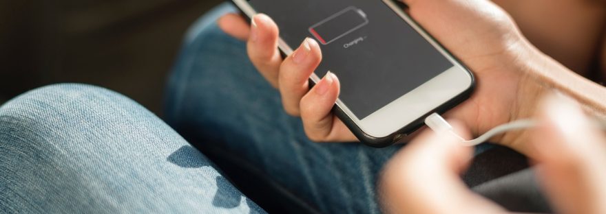 Smartfon z niemal rozładowaną baterią podłączony do ładowania w dłoni.