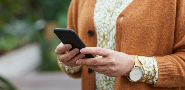 Kobieta w pomarańczowym sweterku trzyma w dłoni telefon
