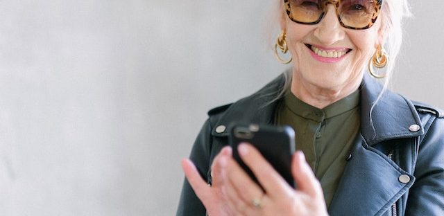 Starsza kobieta w okularach trzyma telefon w dłoni