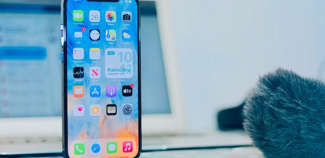 Telefon komórkowy z włączonym wyświetlaczem, w tle laptop